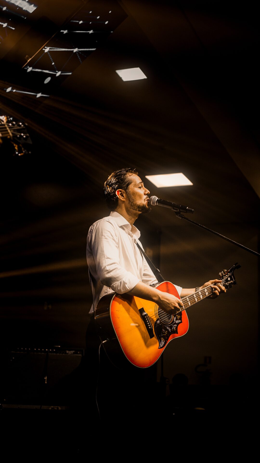 Rodolfo Santos cantor no palco com iluminação quente em Maringá